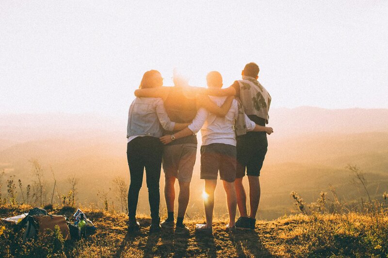 Team of four people standing together at sunset, arms around each other, representing collaboration and unity at Calling All Minds